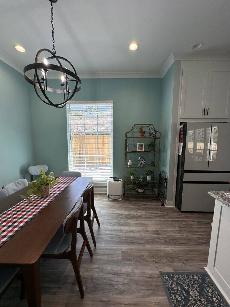 Modern dining room with freshly painted teal walls, wood floors, and orb chandelier.